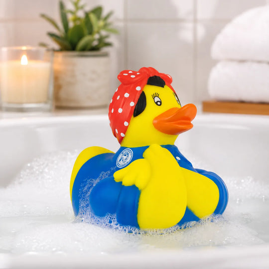 A yellow rubber duck wearing a red polka-dot headscarf and blue swimsuit, floating in a bubble-filled bathtub with a lit candle and potted plant in the background.