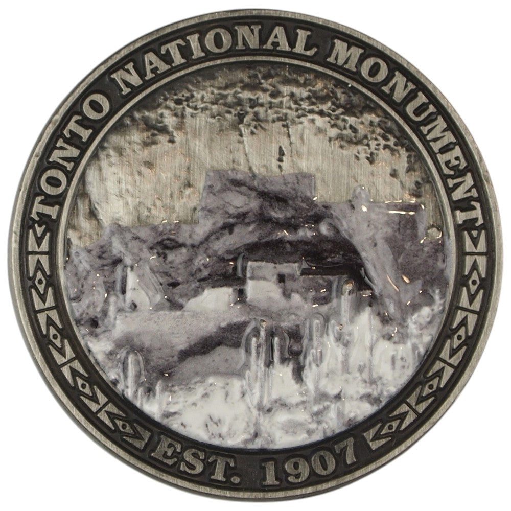 Metal collectible coin representing Tonto National Monument depicting a cliff dwelling set in a desert scene.