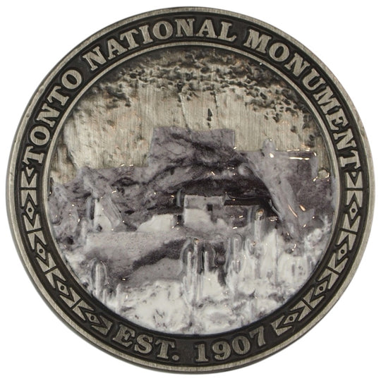 Metal collectible coin representing Tonto National Monument depicting a cliff dwelling set in a desert scene.