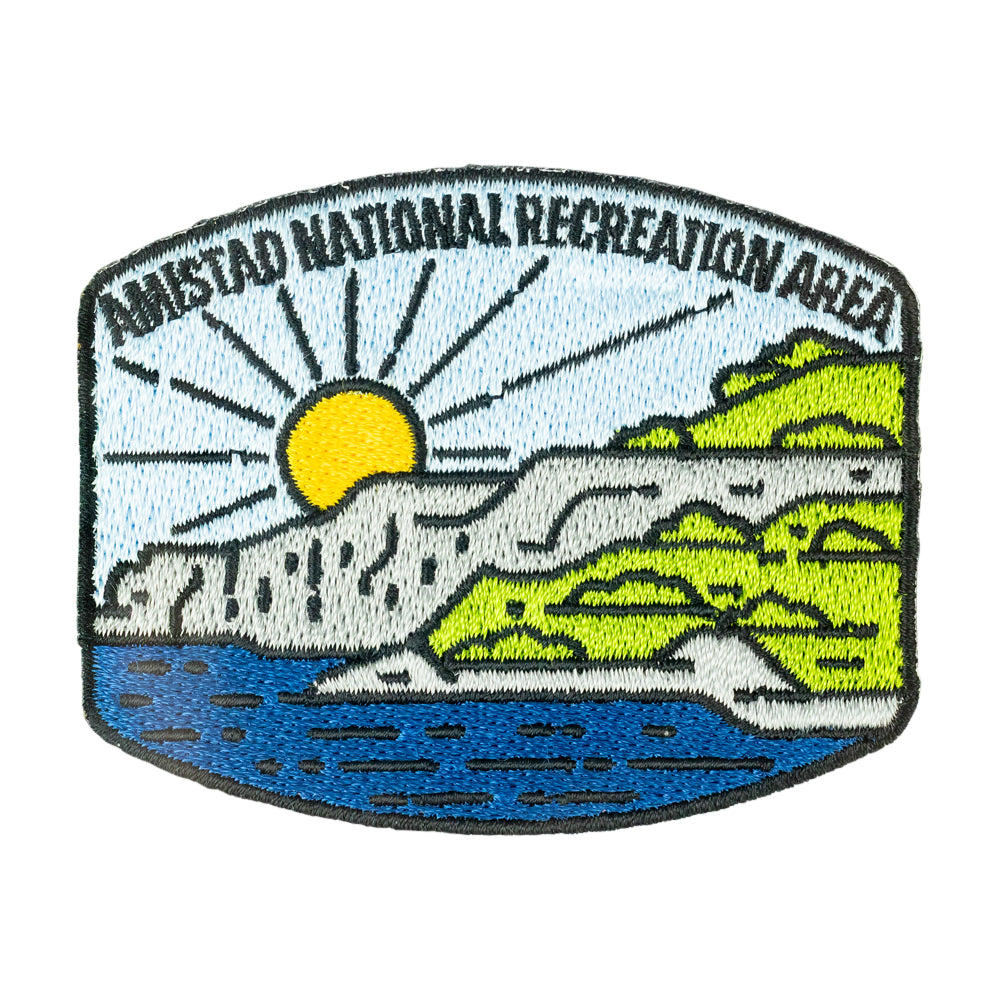 Embroidered patch for Amistad National Recreation Area featuring a stylized landscape with a yellow sun, blue water, green hills, and gray rocks on a white background.