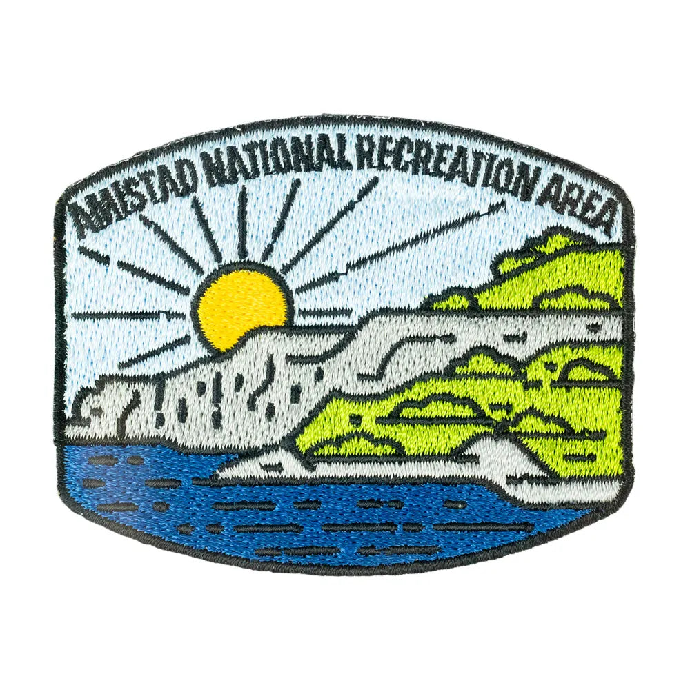 Embroidered patch for Amistad National Recreation Area featuring a stylized landscape with a yellow sun, blue water, green hills, and gray rocks on a white background.