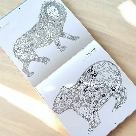 Coloring book with intricate lion and capybara designs on a wooden surface