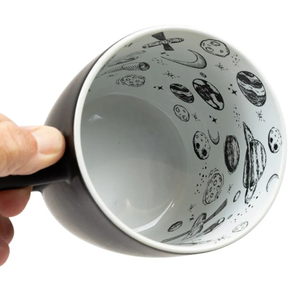 Ceramic mug with space-themed design held by a hand on a white background