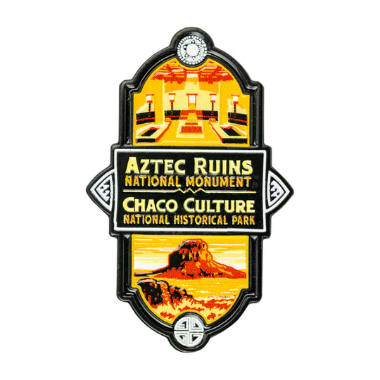 A vintage-style enamel pin or featuring Aztec Ruins National Monument and Chaco Culture National Historical Park graphics, with a black border and yellow, orange, and red illustrated scenes on a white background.
