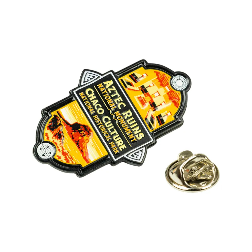 An Aztec Runs National Monument lapel pin featuring Chaco Culture National Historic Site imagery, shown next to its gold-tone metal clutch backing on a white background.