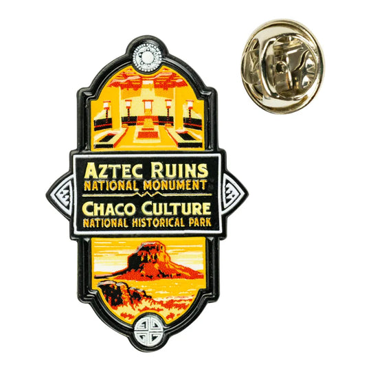 An Aztec Ruins National Monument and Chaco Culture National Historical Park enamel lapel pin shown from the front, with a separate gold-tone metal pin backing visible to the upper right, on a plain white background.