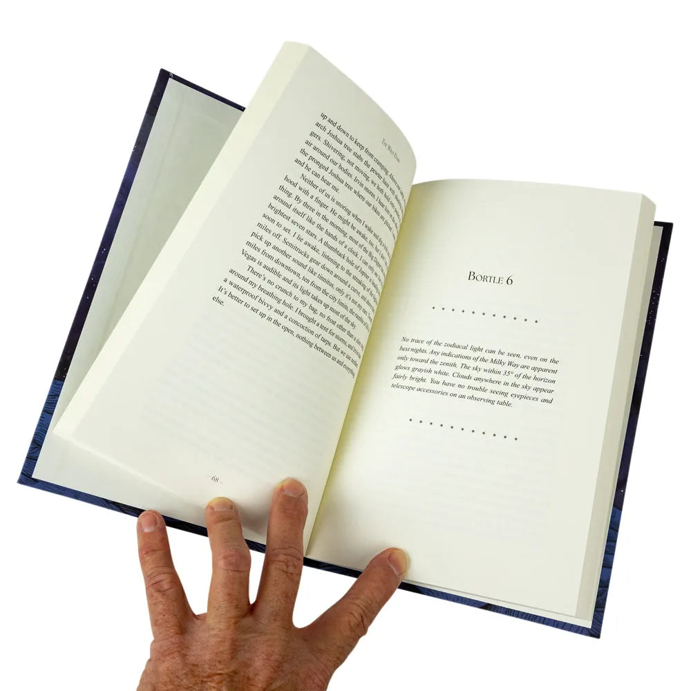 An open book with cream-colored pages and dense text, held open by a hand against a plain white background.