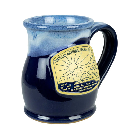 A ceramic mug with a blue gradient glaze, featuring a gold-colored metal badge on the side that reads &