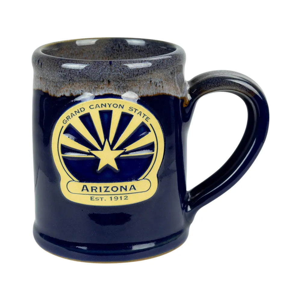 A dark blue ceramic mug with a glossy finish, featuring the Arizona state emblem printed in gold on the front. The mug has a rustic, speckled brown glaze around the rim and a sturdy handle, shown against a plain white background.