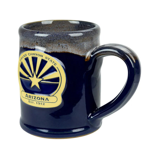 A dark blue glazed ceramic mug featuring the Arizona state flag emblem on the side, with a brown speckled glaze around the rim, shown on a white background.