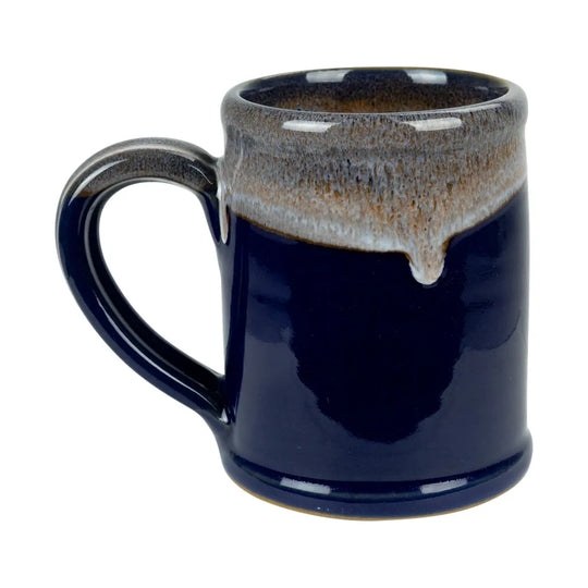 A ceramic mug with a glossy deep navy blue body and a contrasting dripping glaze rim in brown, beige, and white, set against a plain white background.