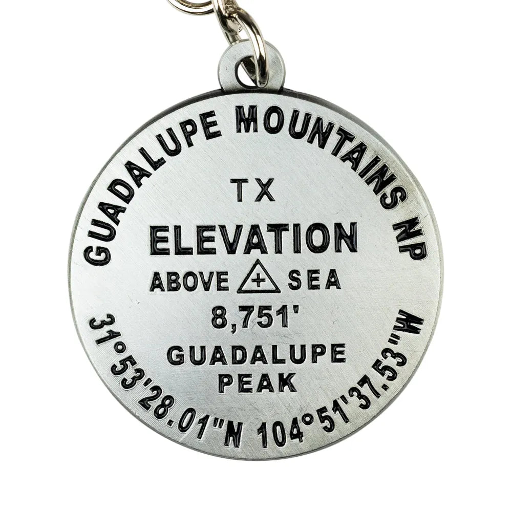 A round silver metal Guadalupe Mountains NP elevation pendant on a white background, featuring engraved black text and a small metal keyring loop at the top.