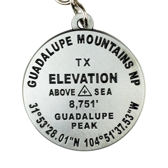 A round silver metal Guadalupe Mountains NP elevation pendant on a white background, featuring engraved black text and a small metal keyring loop at the top.