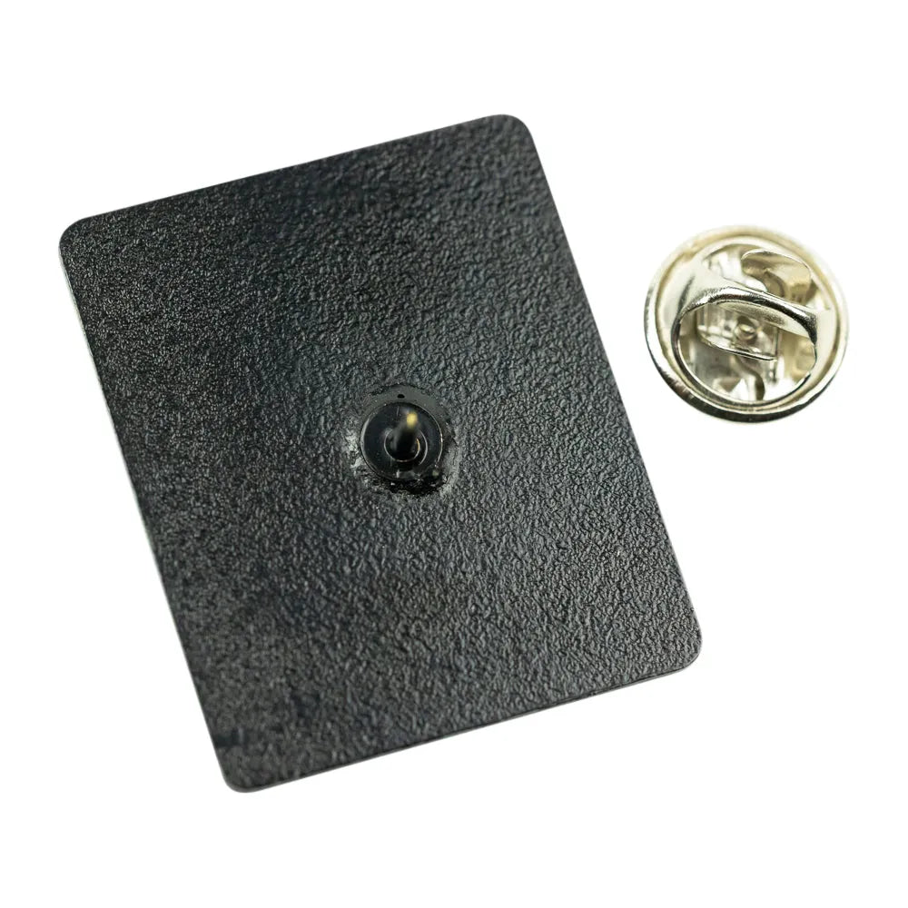 A square black textured pinback badge with a small central metal contact point, shown next to its gold-toned metal clutch backing on a white background.
