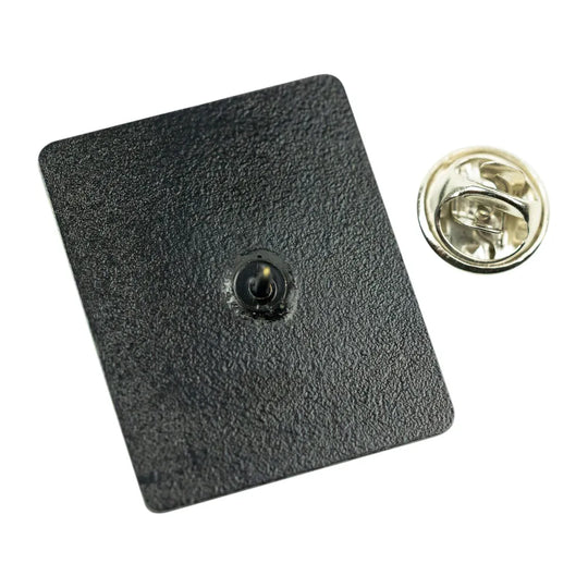 A square black textured pinback badge with a small central metal contact point, shown next to its gold-toned metal clutch backing on a white background.