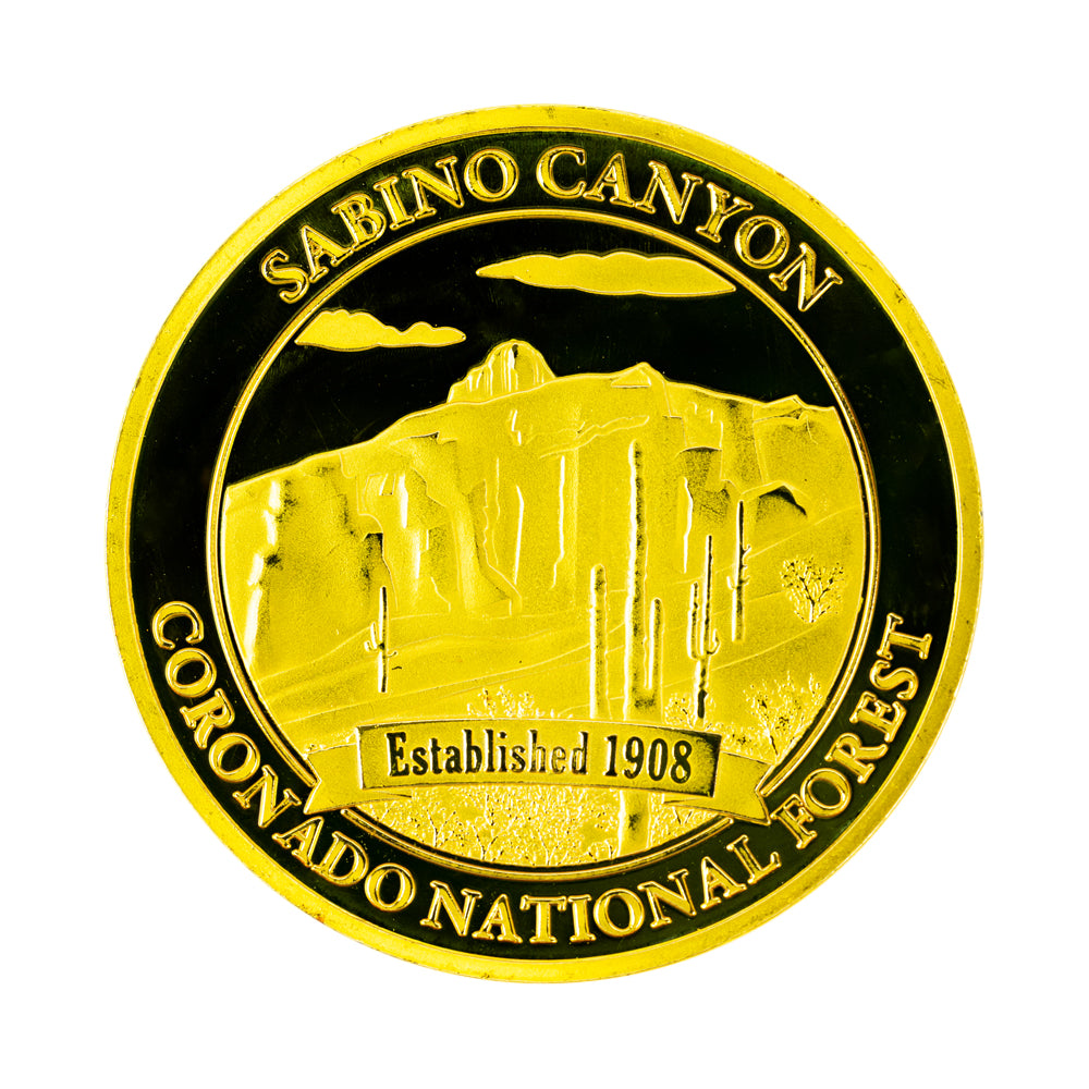 A round gold-colored commemorative coin with a depiction of Sabino Canyon with the text &