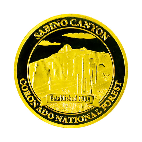 A round gold-colored commemorative coin with a depiction of Sabino Canyon with the text &