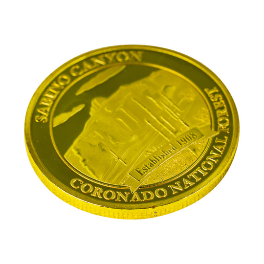A round gold-colored commemorative coin featuring an embossed depiction of Sabino Canyon and the text &