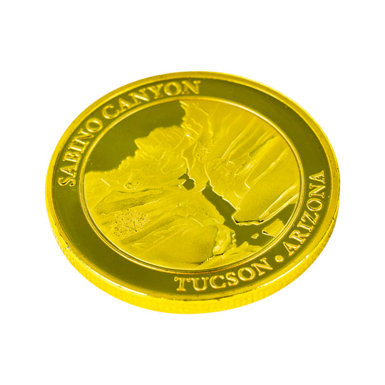A round, metallic gold challenge coin featuring an embossed profile of a canyon and the text &