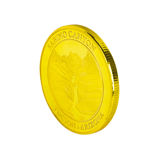 A shiny gold-colored coin featuring a relief of a canyon and the embossed text &