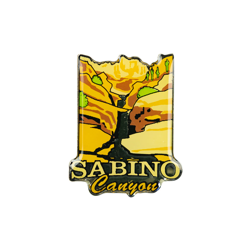 A Sabino Canyon photo dome pin featuring a stylized canyon landscape with yellow and orange rock formations, green trees, and the text &