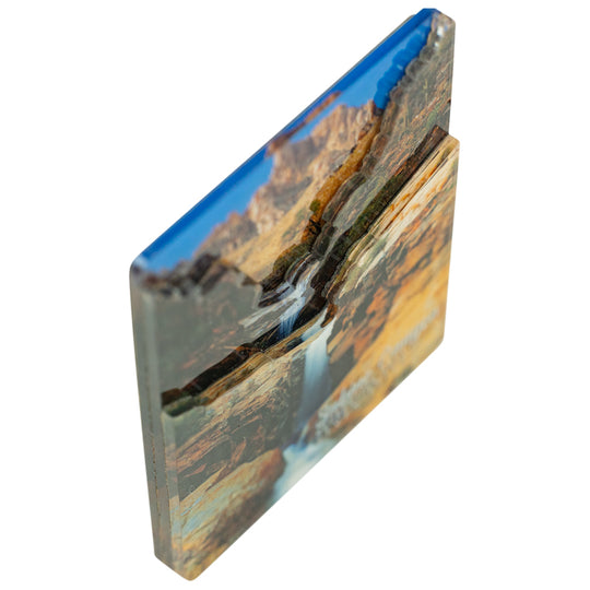 A rectangular magnet featuring a layered landscape design with a blue river flowing through canyon mountains, shown on a plain white background.
