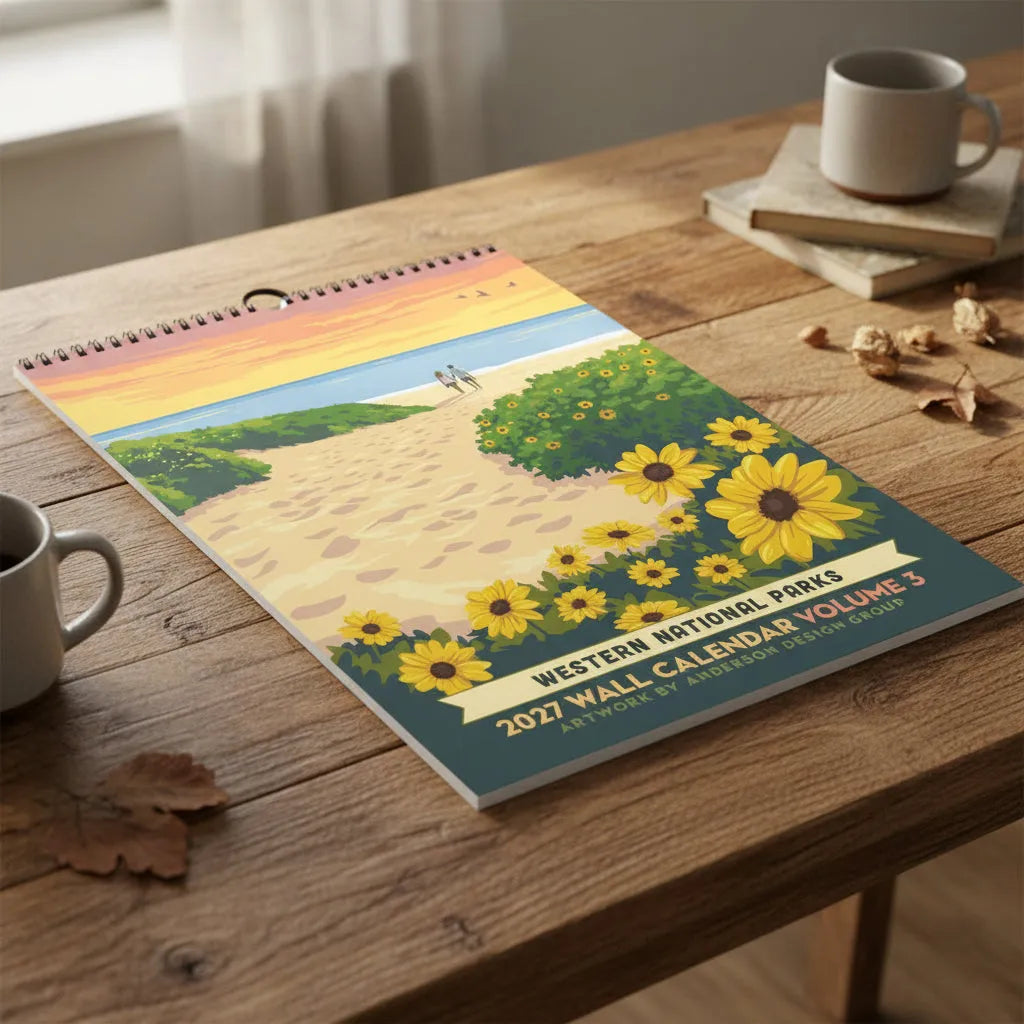 A spiral-bound 2027 Western National Parks wall calendar cover featuring a stylized beach scene with sunflowers, green shrubs, a sandy path, two people walking at the shoreline, and an orange sunset sky.