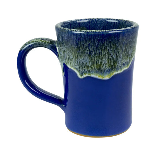 A ceramic coffee mug with a deep cobalt blue body and a textured, dripping glaze on the rim in shades of green and blue, set against a plain white background.