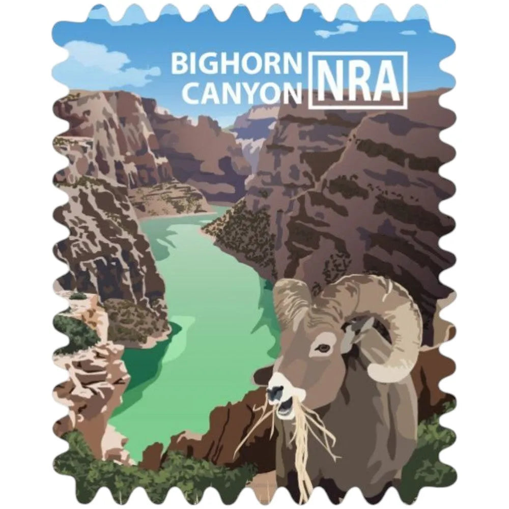 A postage stamp-style illustration of Bighorn Canyon with the text 'BIGHORN CANYON NRA' at the top. The scene shows rocky canyon walls, a turquoise river, and a large bighorn ram in the foreground.