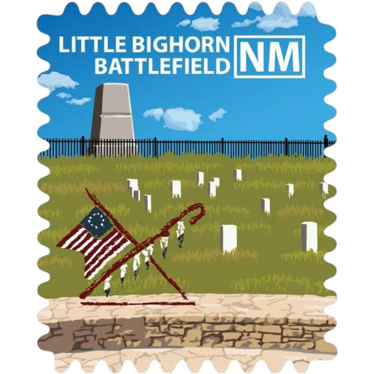 A stamp-style illustration of the Little Bighorn Battlefield in New Mexico, showing a blue sky, grassy field with white headstones, a stone monument, a black fence, and a crossed rifle with an American flag and hanging feathers. The text &