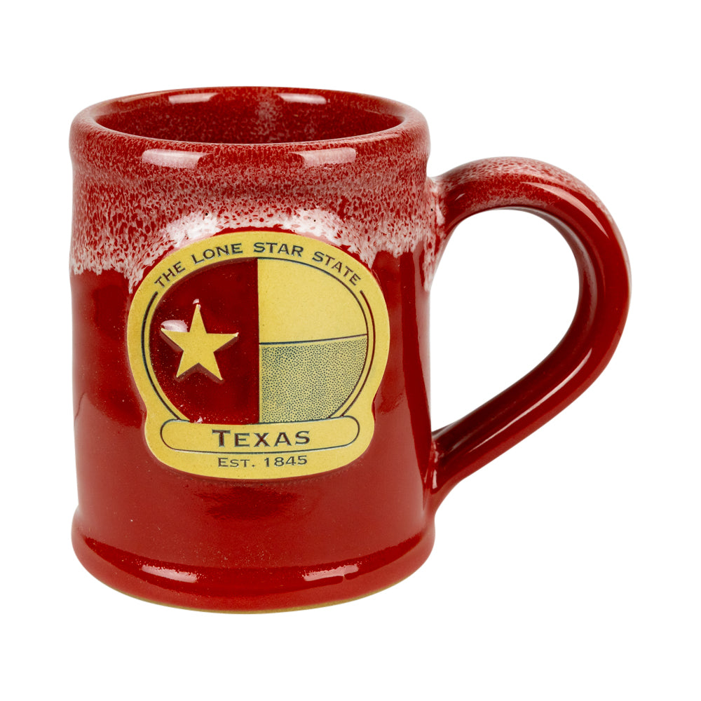 A red ceramic mug with a glossy finish and a distressed white speckled rim, featuring a circular yellow and beige Texas state emblem on the front with the text &
