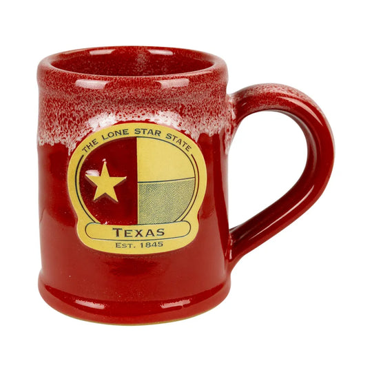 A red ceramic mug with a glossy finish and a distressed white speckled rim, featuring a circular yellow and beige Texas state emblem on the front with the text &