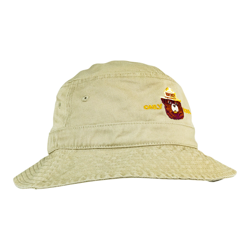 A light beige bucket hat with a small embroidered logo on the front featuring Smokey Bear.