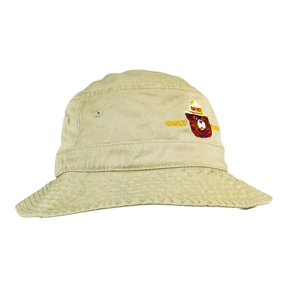 A light beige bucket hat with a small embroidered logo on the front featuring Smokey Bear.