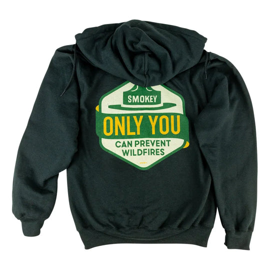 A dark hoodie shown from the back, featuring a large graphic print of a shield-shaped badge with a cowboy hat and the text &