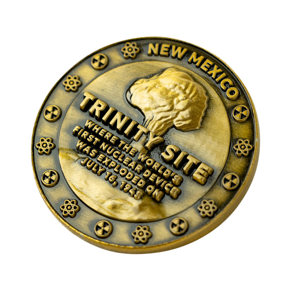 A round bronze-colored commemorative coin featuring a raised profile of a mushroom cloud, the words &