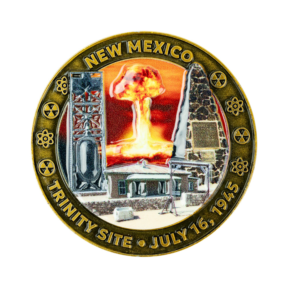 A circular commemorative coin or medallion for the Trinity Site in New Mexico, dated July 16, 1945. The design shows a nuclear explosion mushroom cloud between two tall structures, with surrounding text reading “NEW MEXICO” and “TRINITY SITE • JULY 16, 1945.