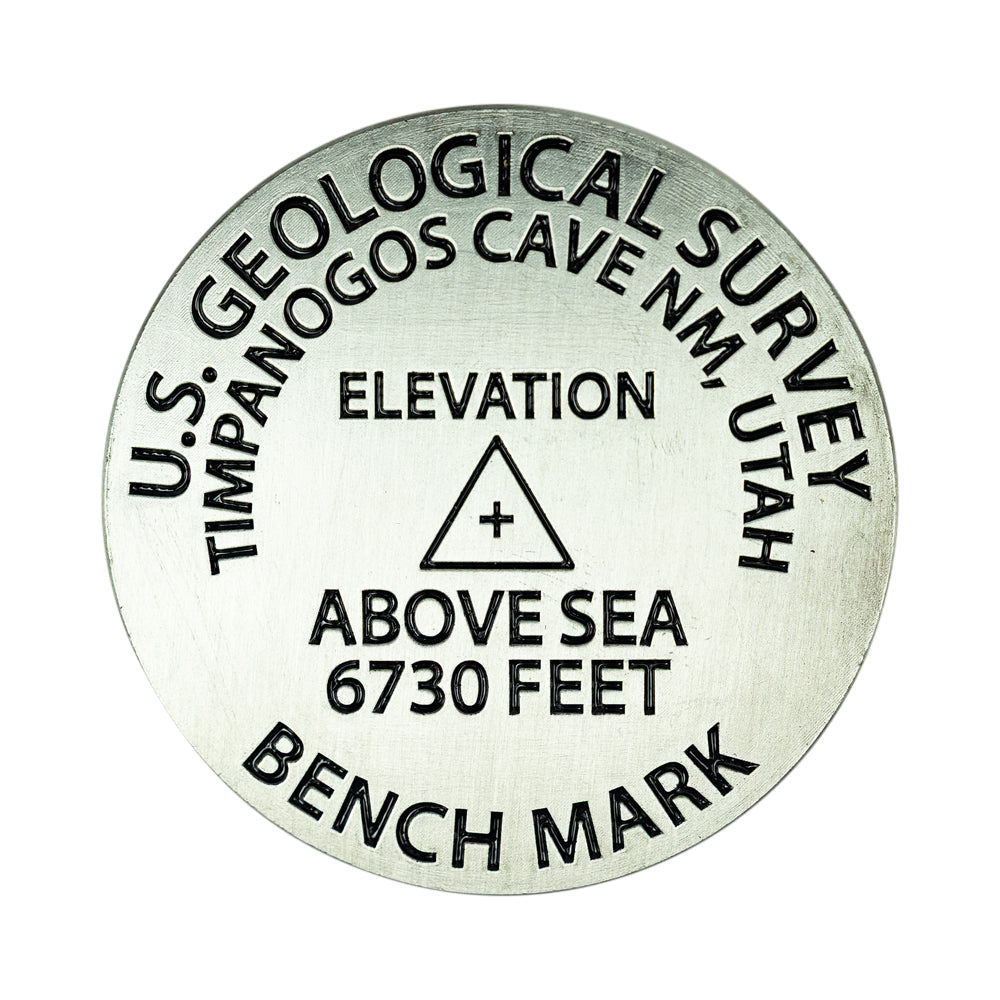 A round metallic geological survey benchmark medallion with black engraved text reading 'U.S.