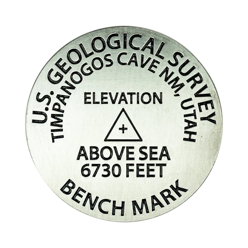 A round metallic geological survey benchmark medallion with black engraved text reading &