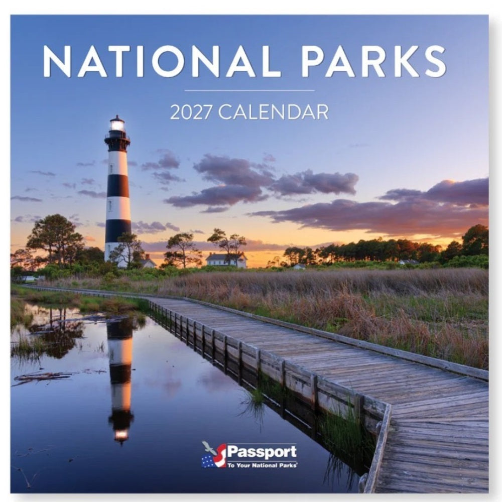 National Parks 2027 Calendar wall art featuring a scenic photograph of a black-and-white lighthouse at sunset beside a boardwalk over calm water, with the title &