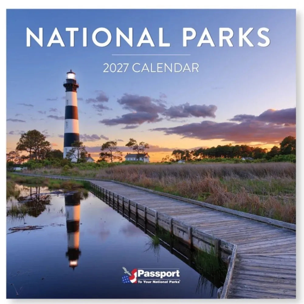 National Parks 2027 Calendar wall art featuring a scenic photograph of a black-and-white lighthouse at sunset beside a boardwalk over calm water, with the title 'NATIONAL PARKS 2027 CALENDAR' at the top and a Passport logo at the bottom.