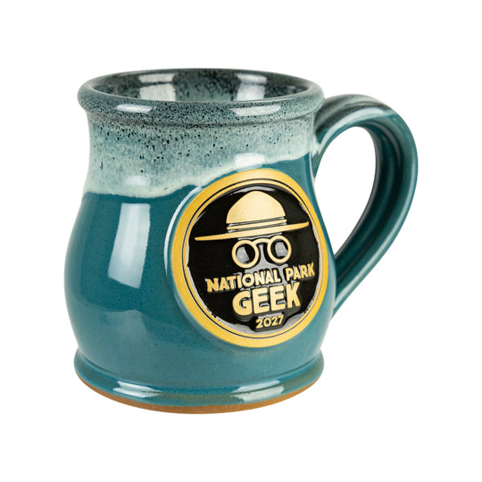 A teal and dark green speckled ceramic mug with a gold and black &