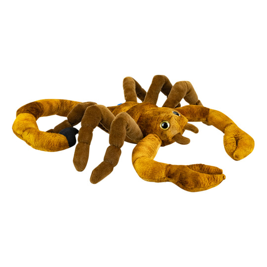 A plush scorpion toy in shades of brown and golden brown, featuring large green eyes and a small black accent on one leg, isolated on a white background.