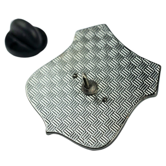 A silver-toned metal badge or pin with a textured diamond pattern and a small black rubber-like piece shown separately on a white background.