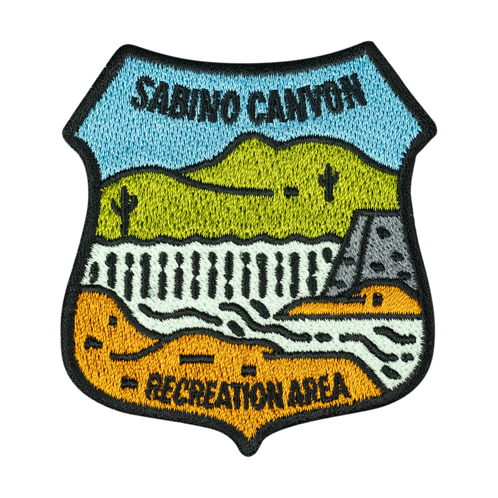 Badge shaped embroidered patch representing Sabino Canyon Recreation Area with simple, stylized landscape image shown on a white background.