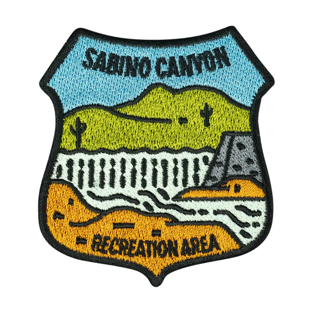 Badge shaped embroidered patch representing Sabino Canyon Recreation Area with simple, stylized landscape image shown on a white background.