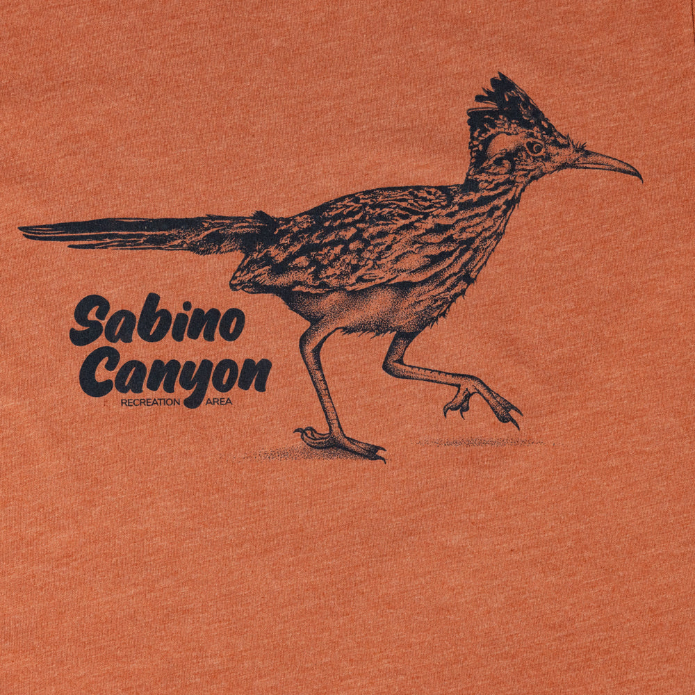 A close-up of an orange heathered fabric surface featuring a black line-art illustration of a roadrunner and the text &