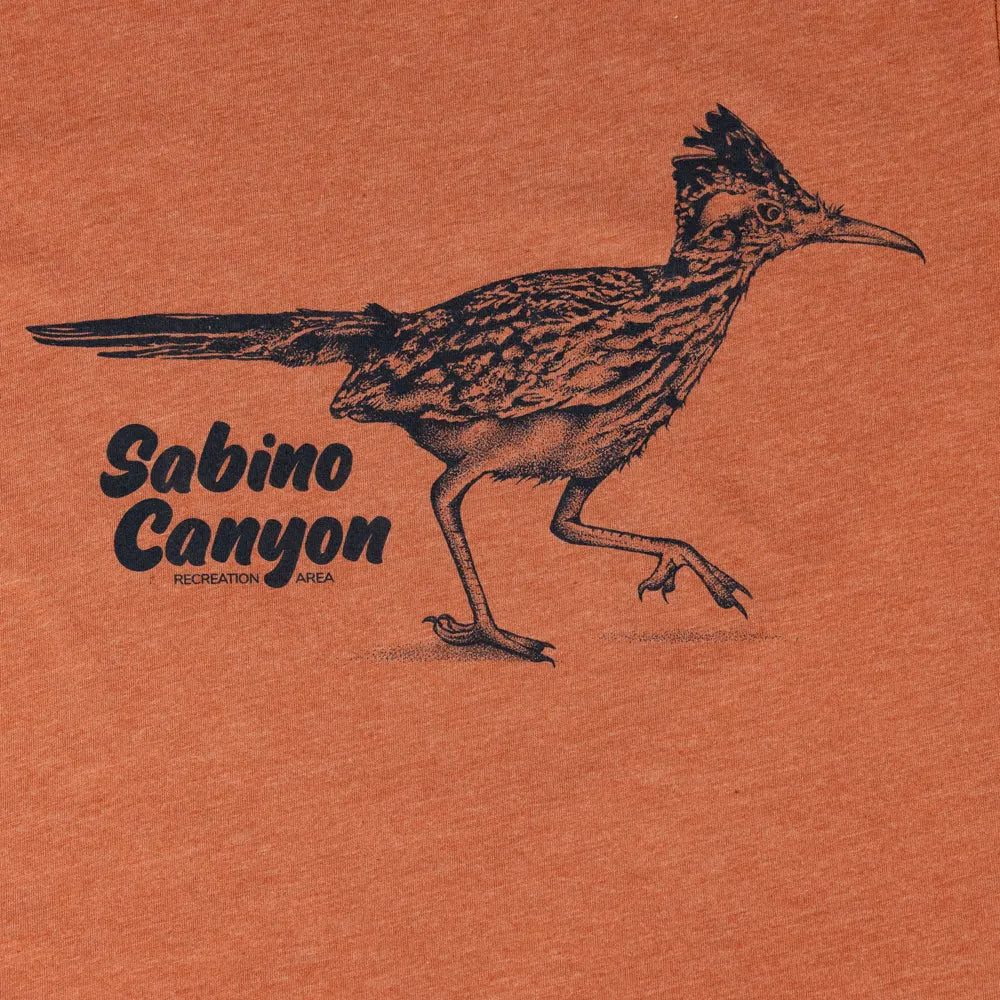 A close-up of an orange heathered fabric surface featuring a black line-art illustration of a roadrunner and the text &