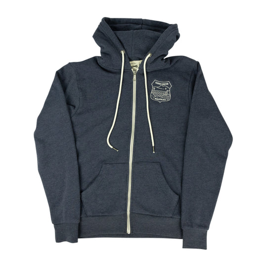 A dark heather gray zip-up hoodie with cream-colored drawstrings and a zipper, featuring a small embroidered shield logo on the left chest, displayed against a solid white background.