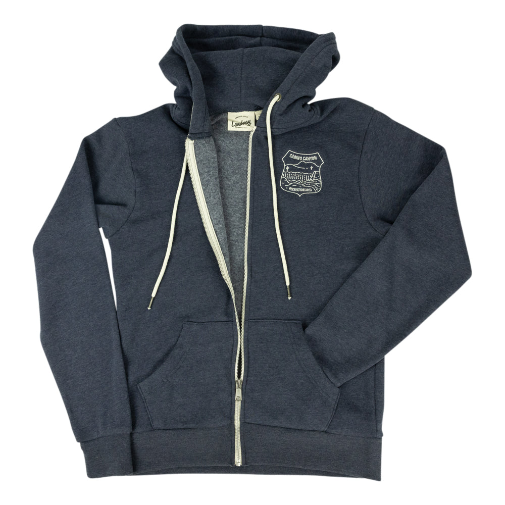 A dark heather gray zip-up hoodie with cream-colored drawstrings and a white embroidered shield logo on the left chest, displayed flat against a white background.